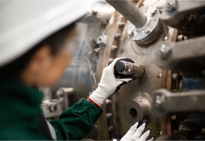 Wearing safety gloves and a hard hat, a person inspects a large industrial machine, utilizing the Ranger Pro Sensor on its surface.